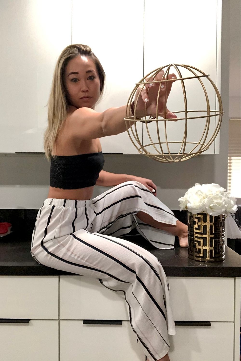 casual spring outfits black tube top and stiped palazzo pants holding gold ball and flowers