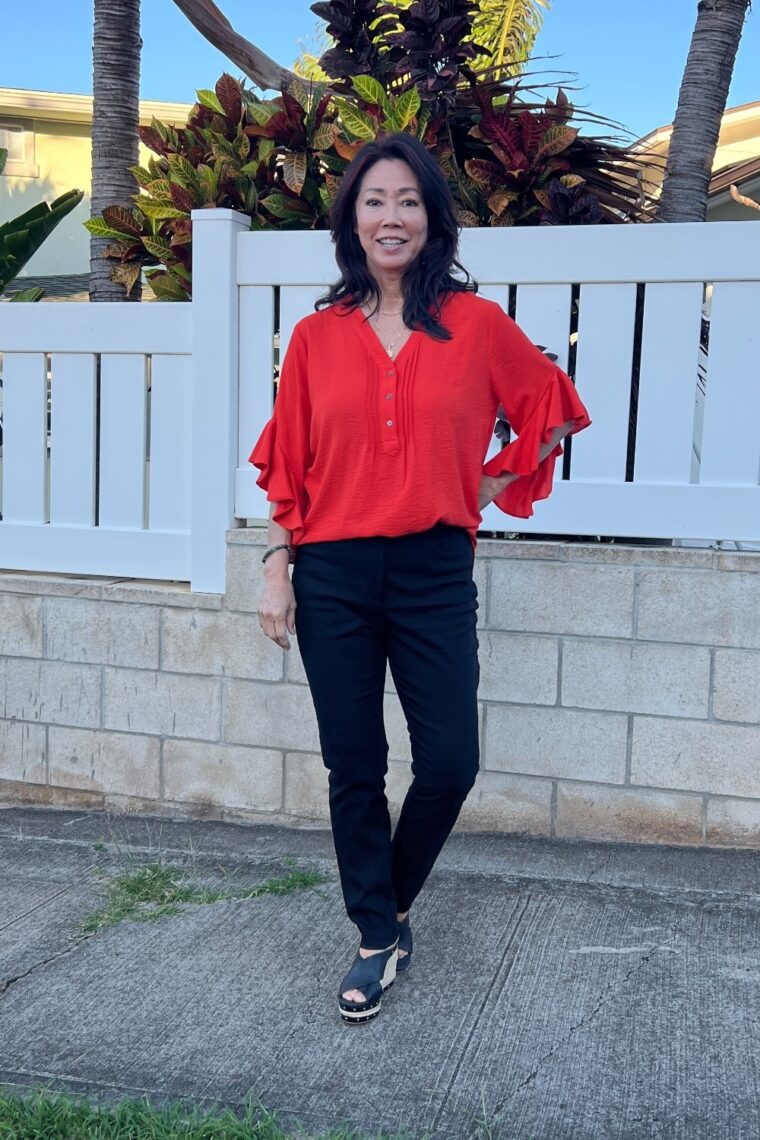 orange flutter sleeve blouse with black pants and black slip on espadrilles